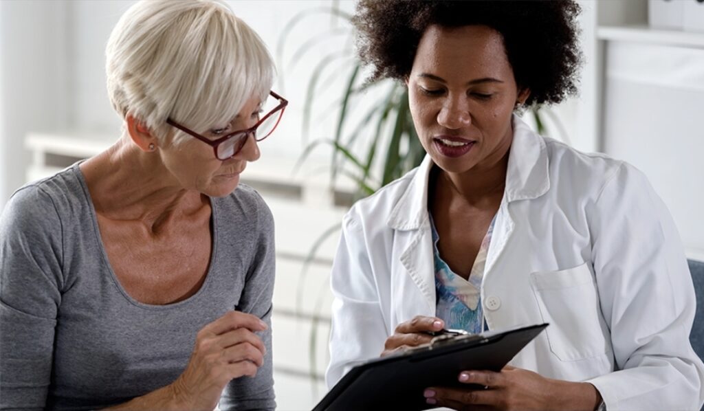 Older woman consulting with a healthcare professional in a white coat, discussing pain management options, including spinal cord stimulators and pain pumps, in a clinical setting.